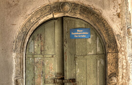 Sehr alte Holztür mit Stein und Schild.